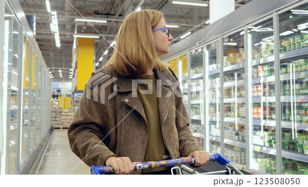 Young woman browsing dairy products in the refrigerated section of a supermarket, pushing a shopping cart 123508050