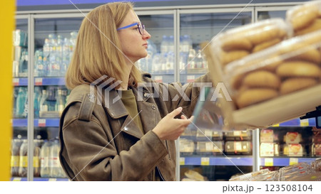 Young lady choosing a loaf of bread from the bakery aisle while making decisions during grocery shopping at the supermarket 123508104