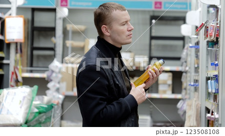 Customer compares detergent products in the household chemical aisle of a supermarket while reading labels. A man chooses hygiene products in a supermarket, shelves with shampoos Customer compares detergent products in the household chemical aisle of a supermarket while reading labels. A man chooses hygiene products in a supermarket, shelves with shampoos 123508108