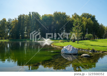 A serene and tranquil pond featuring a beautiful fountain amidst a lush green landscape 123508352