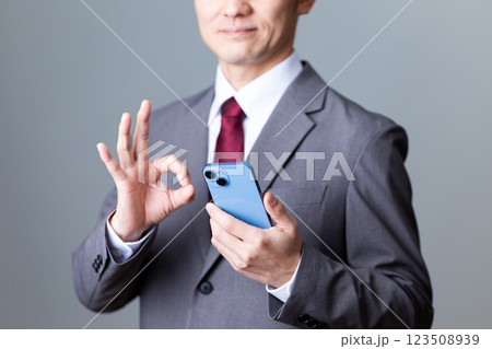 グレーのスーツを着てスマホを持って丸サインをするミドル男性ビジネスマン 123508939