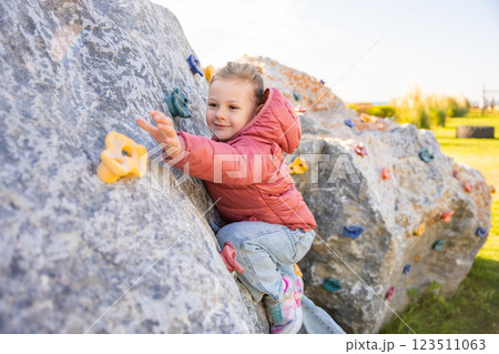 Little girl climbing an artificial climbing wall in a playground, developing strength and coordination 123511063
