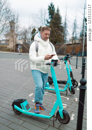 Caucasian man using smartphone app. Male approaches an electric scooter and using mobile phone app NFC contactless locker on bike bicycle in sharing parking lot. Ecological transportation 123511117