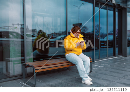 Portrait of happy smiling Caucasian woman, sitting outdoors near building, using smartphone. Technology concept. 123511119