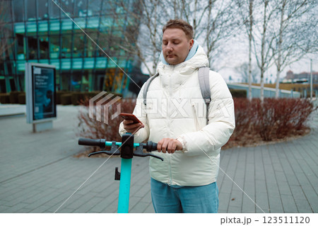 Handsome man using smartphone app. Guy approaches an electric scooter and using mobile phone app NFC contactless locker on bike bicycle in sharing parking lot. 123511120