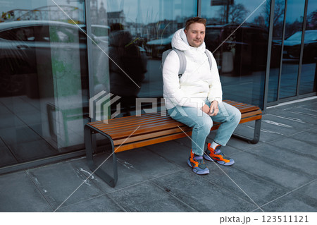 Smiling young white man in casual cothes using mobile phone outdoors in the city, sitting on a bench 123511121