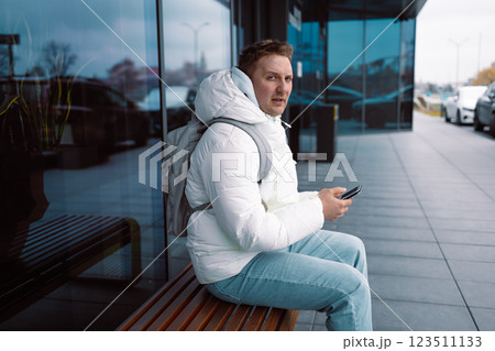 Angry young white man in casual cothes using mobile phone outdoors in the city, sitting on a bench Angry young white man in casual cothes using mobile phone outdoors in the city, sitting on a bench 123511133