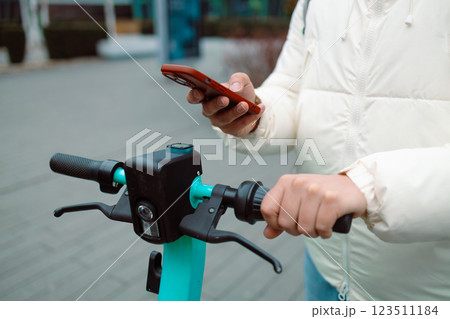 Handsome man using smartphone app. Guy approaches an electric scooter and using mobile phone app NFC contactless locker on bike bicycle in sharing parking lot. 123511184