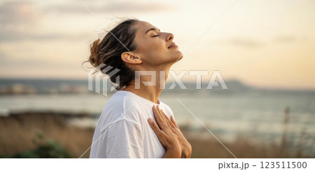 A close profile shot of a person gently placing their hand on their chest while taking a deep breath. This highlights the connection between breath and physical sensation. 123511500
