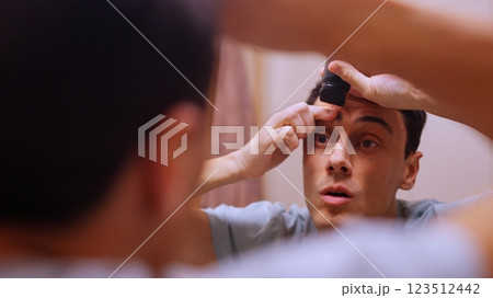 Young man removing eyebrows with electric razor in bathroom mirror 123512442