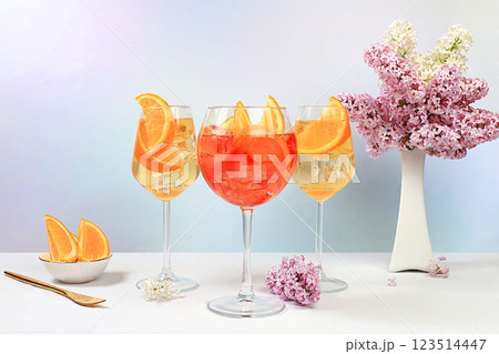 Festive alcoholic cocktail Aperol spritz in glasses on a bright background with a bouquet of lilacs, summer bar concept, alcoholic drinks at a party, restaurant and cafe advertising, selective focus Festive alcoholic cocktail Aperol spritz in glasses on a bright background with a bouquet of lilacs, summer bar concept, alcoholic drinks at a party, restaurant and cafe advertising, selective focus 123514447