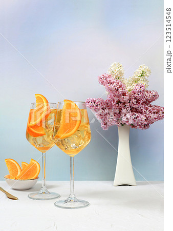 Festive alcoholic cocktail Aperol spritz in glasses on a bright background with a bouquet of lilacs, summer bar concept, alcoholic drinks at a party, restaurant and cafe advertising, selective focus 123514548