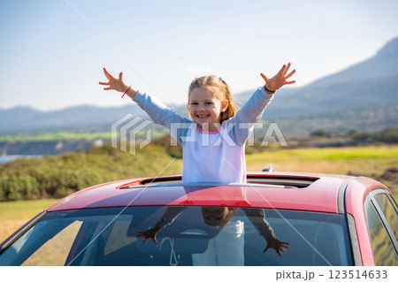 Little girl joyfully sticks out of car sunroof with raised hands against the backdrop of mountains in Northern Cyprus. The image symbolizes freedom, adventure, and the excitement of travel with child 123514633