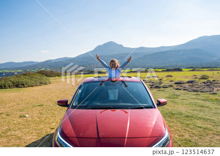 Little girl joyfully sticks out of car sunroof with raised hands against the backdrop of mountains in Northern Cyprus. The image symbolizes freedom, adventure, and the excitement of travel with child 123514637