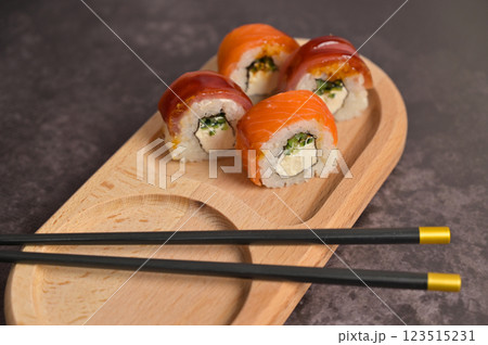 Set of sushi roll with rice and fish and chopsticks on wooden serving board. Dark black texture background with copy space. Close up. Japan menu. Asian food Set of sushi roll with rice and fish and chopsticks on wooden serving board. Dark black texture background with copy space. Close up. Japan menu. Asian food 123515231