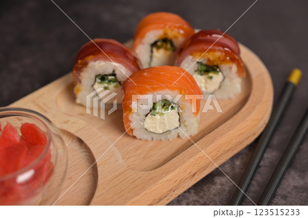 Set of sushi roll with rice and fish, ginger into glass bowl on wooden serving board, chopsticks. Dark black texture background with copy space. Close up. Japan menu. Asian food Set of sushi roll with rice and fish, ginger into glass bowl on wooden serving board, chopsticks. Dark black texture background with copy space. Close up. Japan menu. Asian food 123515233
