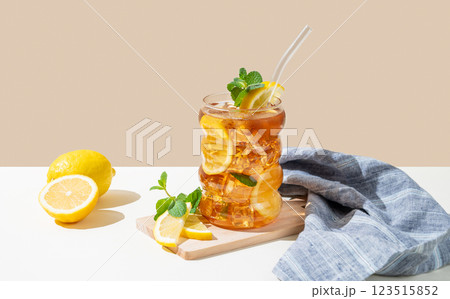 Iced tea with lemon, ice and mint in a glass on beige and white background with shadow and fruits. Iced tea with lemon, ice and mint in a glass on beige and white background with shadow and fruits. 123515852