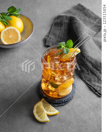 Iced tea with lemon, ice and mint in a glass on gark gray background with citrus fruits and napkin. 123515854