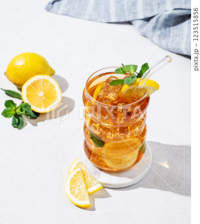 Iced tea with lemon, ice and mint in a glass on light  background with shadow, citrus fruits  123515856