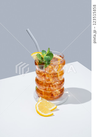 Iced tea with lemon, ice and mint in a glass on white and blue background with shadow. 123515858