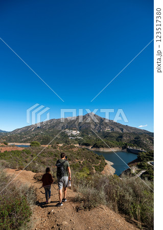 Father and daughter hiking on mountain trail near scenic lake under clear blue sky, La Concepcion 123517380