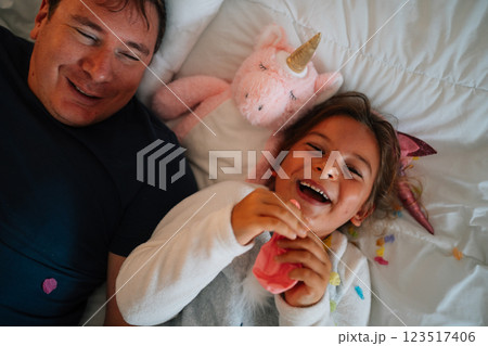 Joyful caucasian adult male and child laughing with unicorn toy on bed 123517406