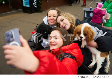 Friends enjoy a winter outing while taking a selfie with their dogs in a festive outdoor location Friends enjoy a winter outing while taking a selfie with their dogs in a festive outdoor location 123518482