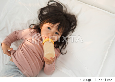 toddler girl drinking milk from bottle on bed toddler girl drinking milk from bottle on bed 123521462