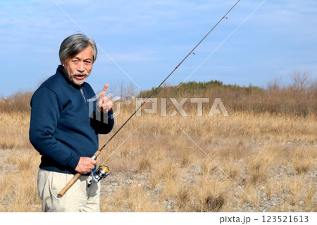 広い河川敷を歩いて流れに向かうベテラン釣り師 広い河川敷を歩いて流れに向かうベテラン釣り師 123521613