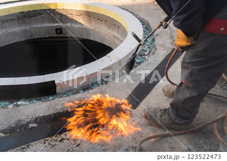 An industrial worker uses fire to soften a rubber underlay for floor insulation, showcasing precision and skill in a critical step of the construction process An industrial worker uses fire to soften a rubber underlay for floor insulation, showcasing precision and skill in a critical step of the construction process 123522473