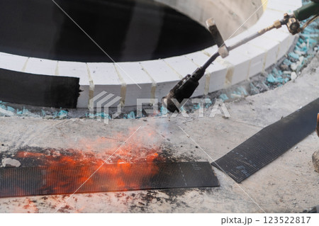 An industrial worker uses fire to soften a rubber underlay for floor insulation, showcasing precision and skill in a critical step of the construction process 123522817
