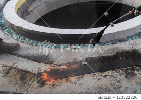 An industrial worker uses fire to soften a rubber underlay for floor insulation, showcasing precision and skill in a critical step of the construction process 123522820