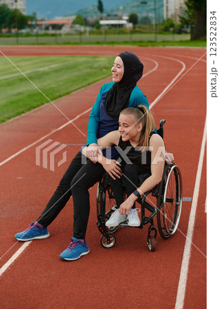 A Muslim woman wearing a burqa resting with a woman with disability after a hard training session on the marathon course 123522834