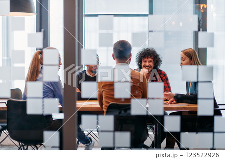 In a sleek glass office space, a team of business professionals engage in lively discussions and exchange strategic ideas, showcasing collaboration and innovation at the heart of modern corporate 123522926