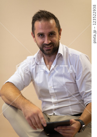 A confident businessman sitting and using laptop with a determined expression, while a beige background enhances the professional atmosphere, showcasing his productivity and expertise. 123522938