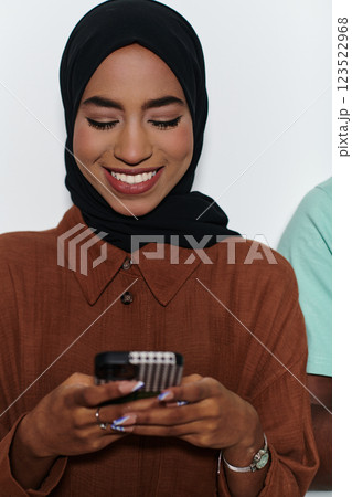 An elegant Arab woman, adorned in a hijab, engages with modernity as she uses a smartphone, the juxtaposition of traditional attire against contemporary technology captured in the isolated setting An elegant Arab woman, adorned in a hijab, engages with modernity as she uses a smartphone, the juxtaposition of traditional attire against contemporary technology captured in the isolated setting 123522968
