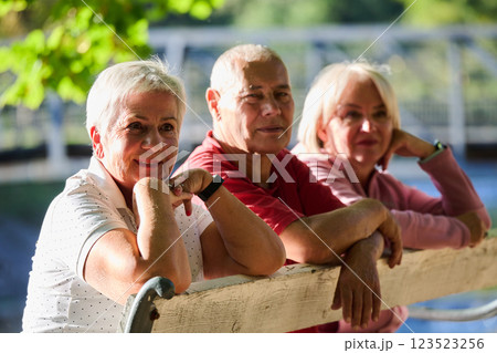 A group of elderly individuals, including a senior man and two older women, sits in a park on a sunny autumn day, embodying the concept of healthy aging through companionship, relaxation, and outdoor 123523256