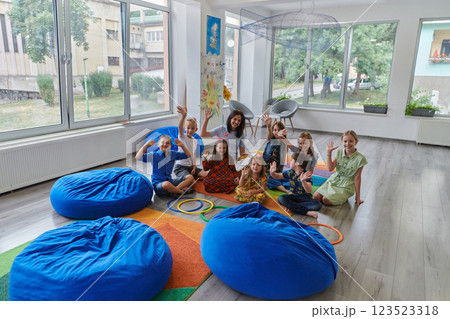 A happy female teacher sitting and playing hand games with a group of little schoolchildren A happy female teacher sitting and playing hand games with a group of little schoolchildren 123523318