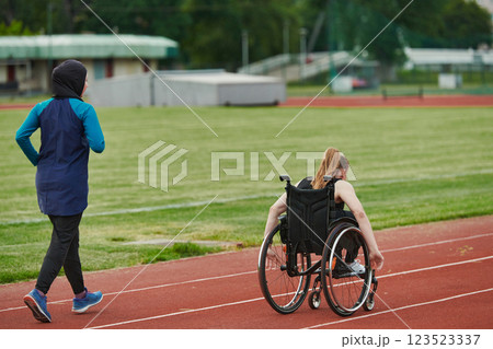 A Muslim woman in a burqa running together with a woman in a wheelchair on the marathon course, preparing for future competitions. A Muslim woman in a burqa running together with a woman in a wheelchair on the marathon course, preparing for future competitions. 123523337
