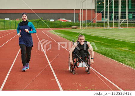 A Muslim woman in a burqa running together with a woman in a wheelchair on the marathon course, preparing for future competitions. A Muslim woman in a burqa running together with a woman in a wheelchair on the marathon course, preparing for future competitions. 123523418