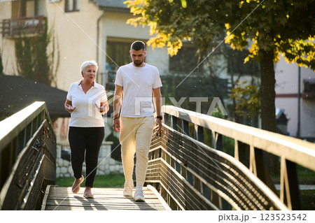 A handsome man and an older woman share a serene walk in nature, crossing a beautiful bridge against the backdrop of a stunning sunset, embodying the concept of a healthy and vibrant intergenerational 123523542