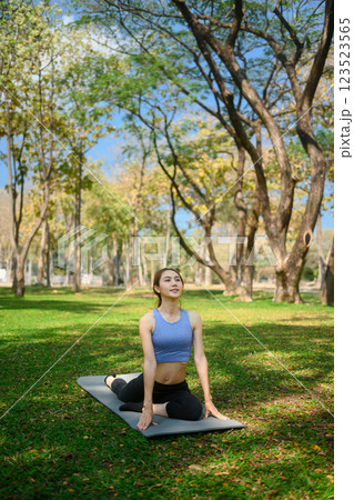 Young woman practicing yoga outdoors in a park, sitting in Half Pigeon yoga pose on mat Young woman practicing yoga outdoors in a park, sitting in Half Pigeon yoga pose on mat 123523565