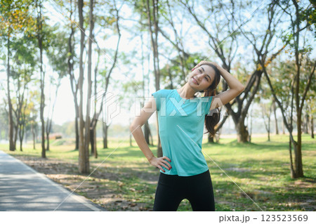 Smiling young woman in sportswear stretching her neck after run in a peaceful park Smiling young woman in sportswear stretching her neck after run in a peaceful park 123523569