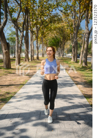 Full length portrait of smiling young woman jogging in a scenic park 123523570