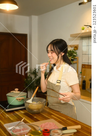 Young Asian woman checking the doneness of her spaghetti in cozy kitchen 123523601