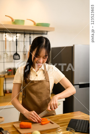 Pretty young woman chopping carrots for her spaghetti sauce in a modern kitchen 123523603
