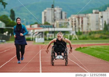 A Muslim woman in a burqa running together with a woman in a wheelchair on the marathon course, preparing for future competitions. 123523666