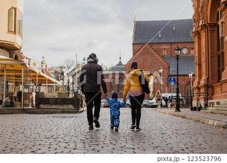 Parents walking hand in hand with their son through the charming city streets, enjoying the warmth of the season and creating joyful memories together Parents walking hand in hand with their son through the charming city streets, enjoying the warmth of the season and creating joyful memories together 123523796