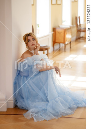 Young woman in blue evening dress sits tiredly or upset on the floor leaning against the wall 123524223