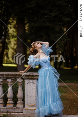 Romantic Woman in a Light Blue Gown Posing on a stone balustrade in a picturesque garden. Romantic Woman in a Light Blue Gown Posing on a stone balustrade in a picturesque garden. 123524226
